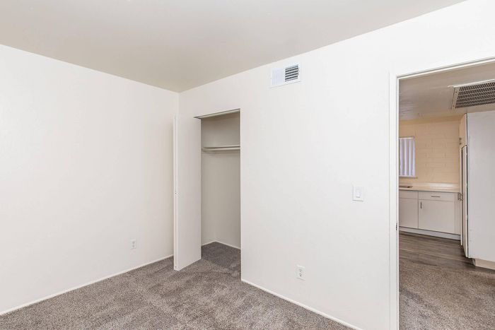 Bright bedroom with plush carpet and a spacious closet, leading to a stylish kitchen with modern cabinetry.