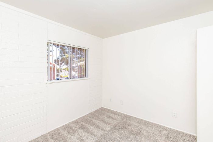 Bright and airy room with crisp white walls, plush carpet, and a large window offering a view of lush greenery, perfect for a cozy living space.