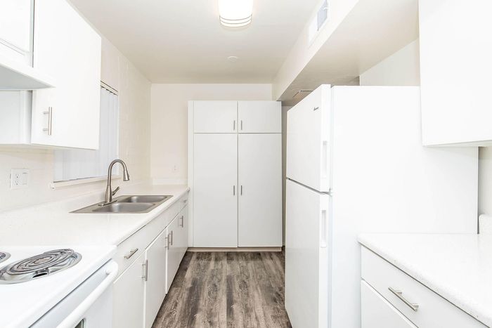 Bright, contemporary kitchen with sleek white cabinetry, modern appliances, and elegant wood-style flooring.
