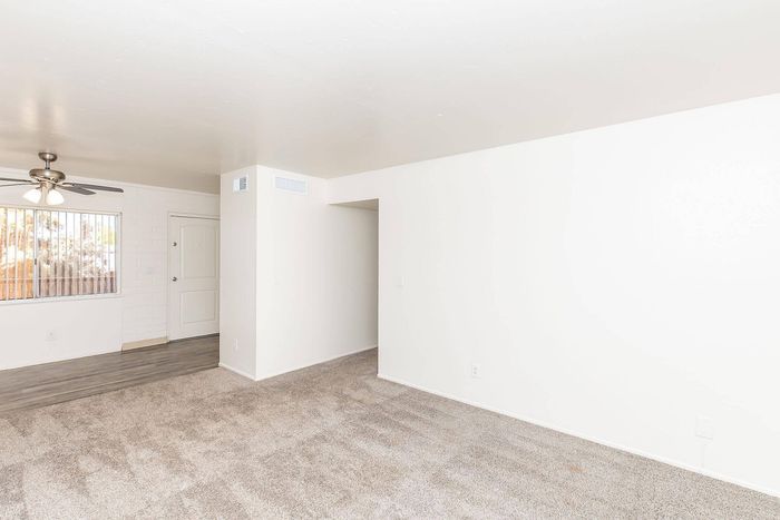 Bright and airy living room featuring elegant carpet flooring, large window with blinds, and a stylish ceiling fan.