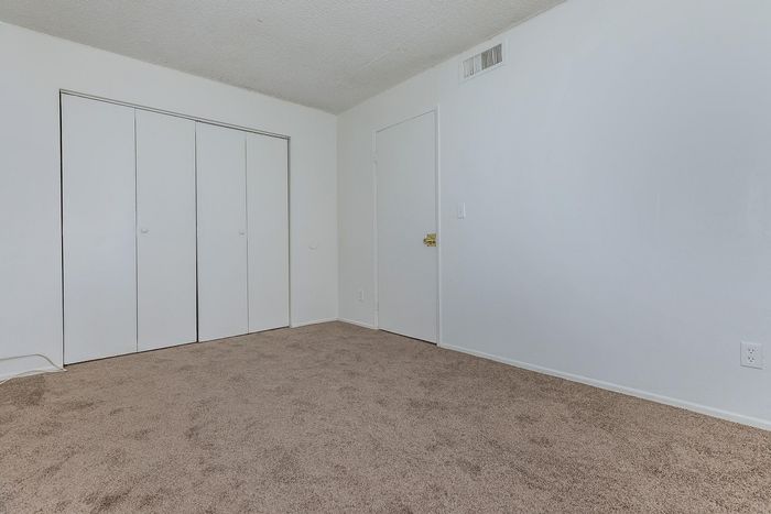 Bright and airy bedroom with plush carpet and ample closet space, featuring sleek white walls for a modern, minimalist vibe.