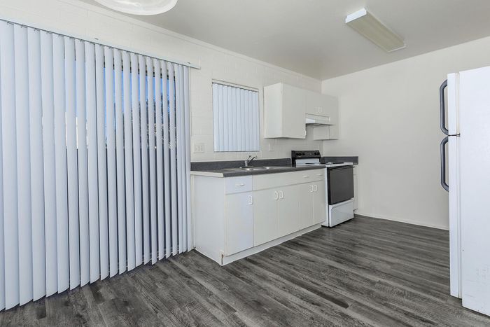 Bright, modern kitchen with sleek white cabinetry, elegant countertops, and stylish flooring, featuring a large window with vertical blinds.