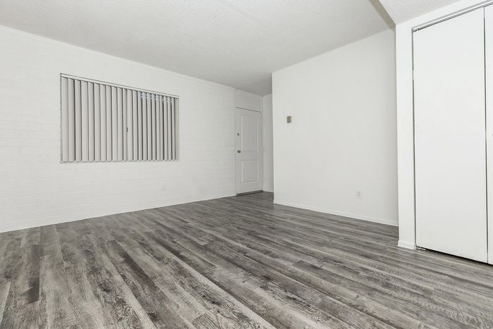 Bright, modern apartment space with stylish gray wood flooring, white walls, and vertical blinds, exuding a fresh and inviting ambiance.