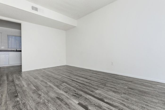 Open living space with sleek hardwood flooring and bright white walls, leading into a modern kitchen area.