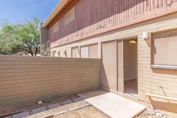 Charming apartment exterior with patio entry, surrounded by stylish brickwork and lush greenery under a clear blue sky.