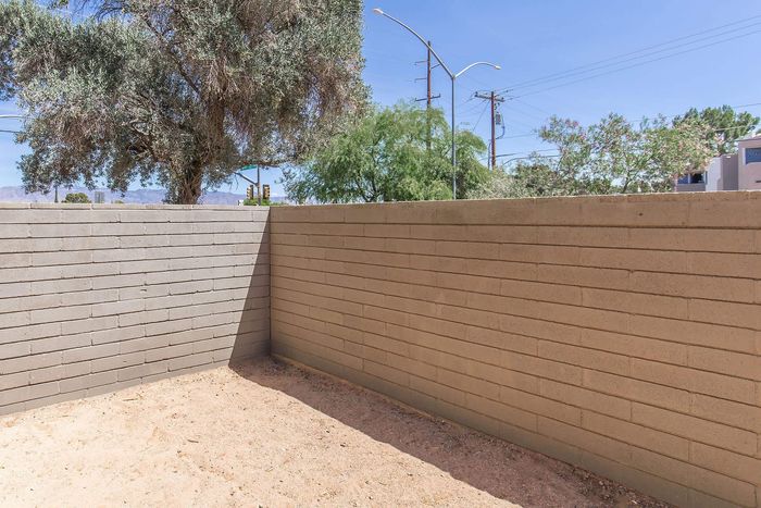 Serene outdoor patio enclosed by a neatly designed brick wall, with natural landscaping and blue skies overhead.