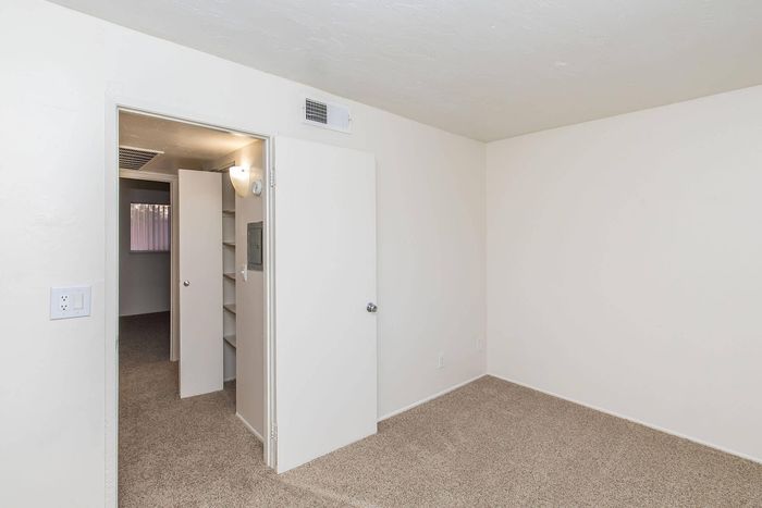 Bright room with soft carpet flooring, neutral tones, and built-in shelving, offering a versatile space in a modern apartment.