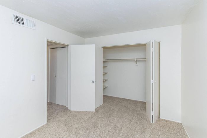 Spacious white closet with ample shelving and hanging space in a beautifully carpeted room.