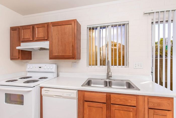 Modern kitchen with sleek wood cabinetry, white countertops, and stainless steel double sink.