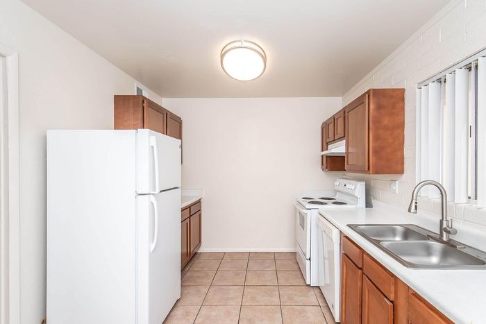Bright and welcoming kitchen featuring rich wooden cabinets, a spacious white countertop, modern appliances, and elegant tile flooring.
