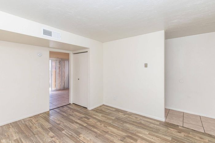 Bright and inviting room with elegant wood flooring, neutral walls, and natural light streaming through vertical blinds.