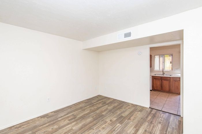 Bright room with elegant hardwood flooring leading to a cozy kitchen featuring wooden cabinets and charming tile work.