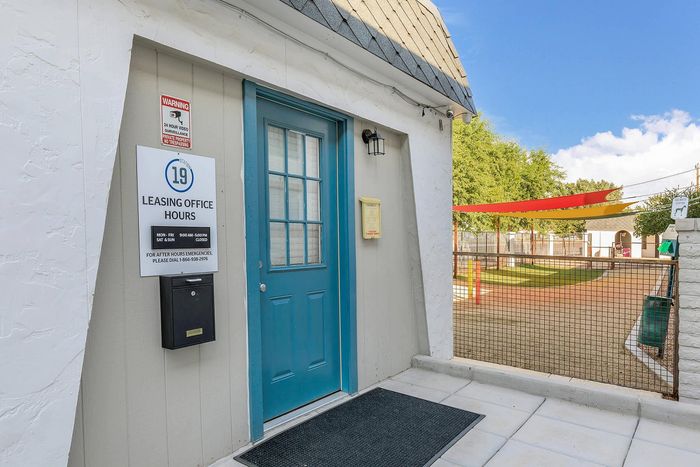 Welcoming leasing office entrance with vibrant blue door and outdoor recreational area, perfect for prospective residents.