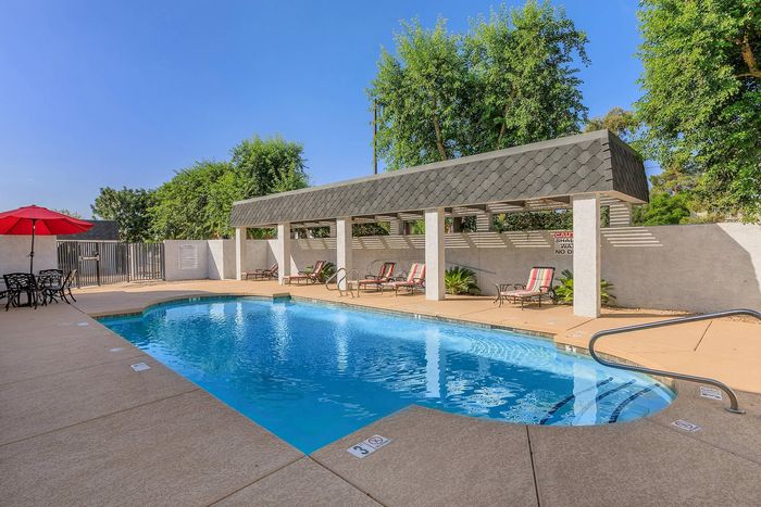 Inviting outdoor pool area with lounge chairs, shaded cabana, and a vibrant red umbrella, perfect for relaxation and enjoyment.