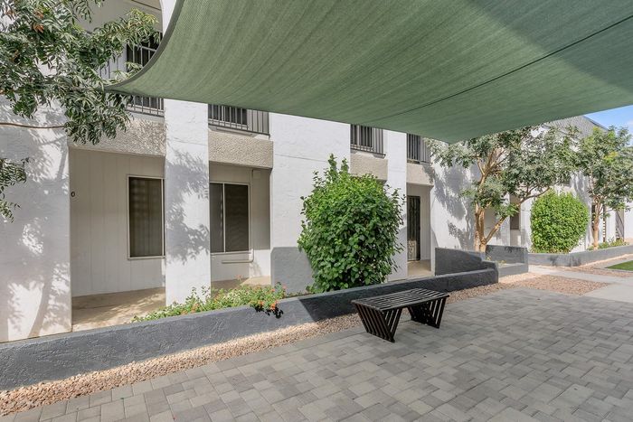 Inviting apartment exterior with modern white facade, lush greenery, and a shaded communal area perfect for relaxation.