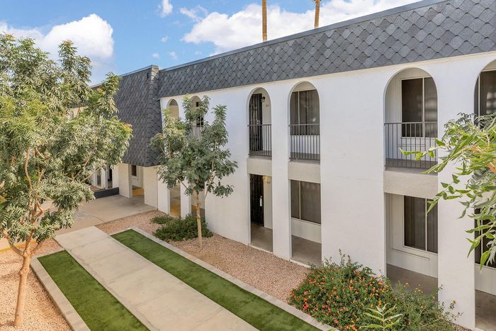 Beautiful two-story apartment building with modern architecture featuring arched balconies, surrounded by lush greenery and a well-maintained pathway.