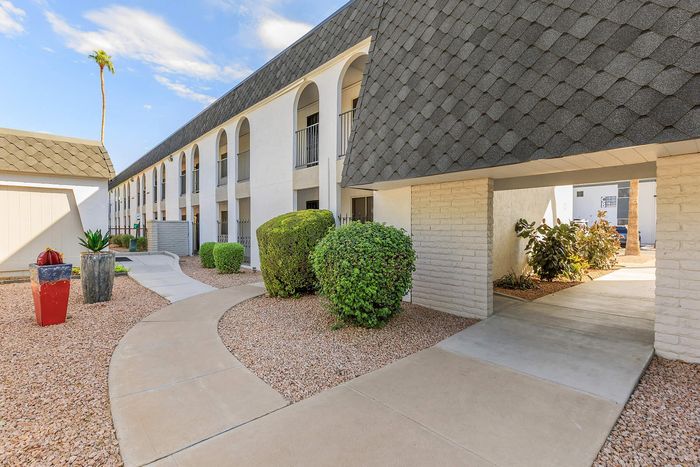 Inviting residential complex with charming archways, modern design, and lush landscaping under a bright blue sky.