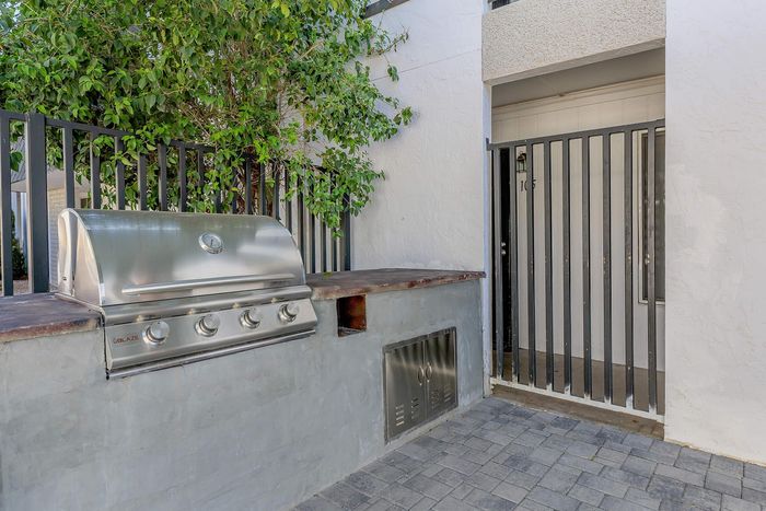 Modern outdoor area featuring a sleek stainless steel BBQ grill next to a stylish gated entrance, surrounded by lush greenery.