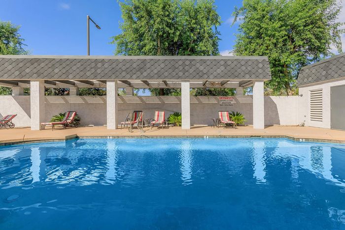 Charming outdoor swimming pool area with lounge chairs, shaded seating, and lush greenery for a relaxing escape.