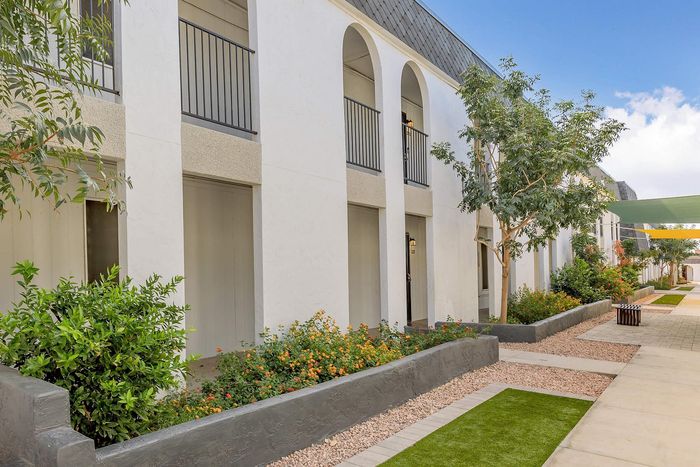 Charming apartment exterior with elegant arches and lush garden pathways under a clear blue sky.