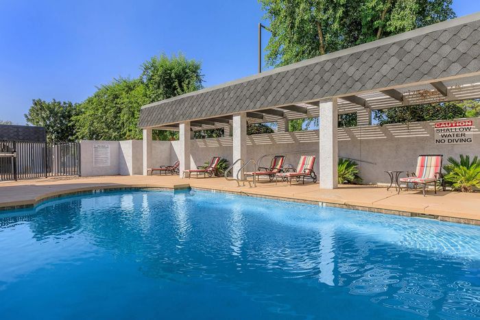 Inviting outdoor pool with stylish lounge chairs and a shaded pergola, surrounded by lush greenery.
