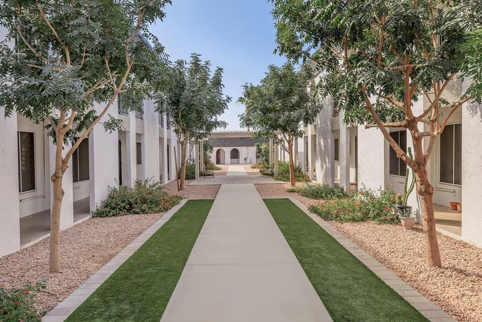 Elegant apartment courtyard with lush greenery and inviting pathways, framed by modern white architecture and vibrant landscaping.
