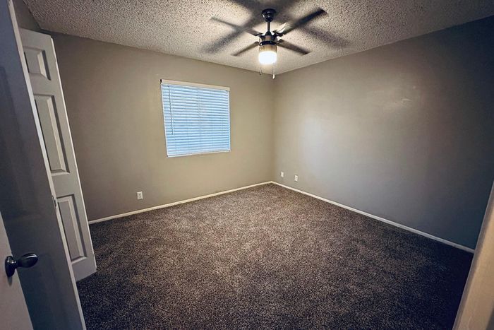 Cozy bedroom with plush carpeting and ceiling fan, filled with natural light from a large window.