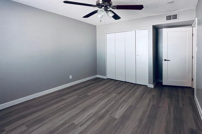 Modern bedroom with sleek wood flooring, ample closet space, and elegant ceiling fan, bathed in natural light.