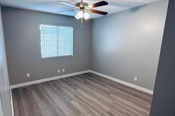 Bright and spacious room featuring elegant flooring, modern ceiling fan, and large window with blinds.