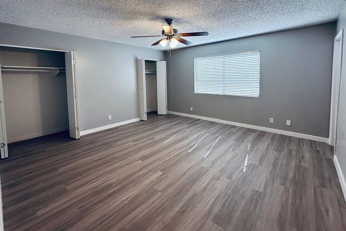 Spacious bedroom with elegant wood flooring, ample closet space, and a modern ceiling fan.