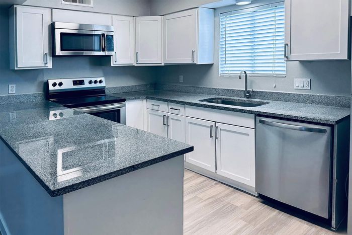 Modern kitchen with sleek granite countertops, stainless steel appliances, and white cabinetry beneath a bright window.