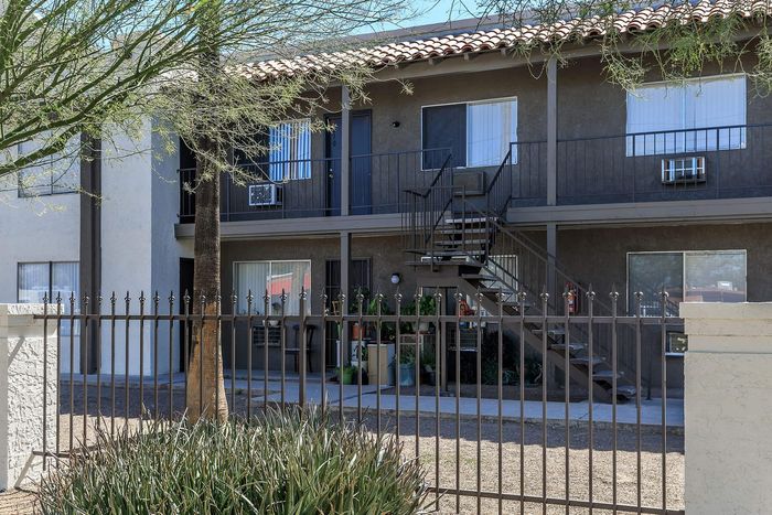 Charming two-story apartment complex with inviting balconies, lush greenery, and secure gated entry.