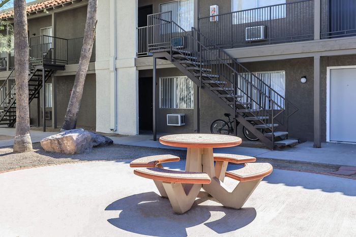 Charming apartment complex with outdoor seating and stair access, complemented by palm trees and a serene atmosphere.