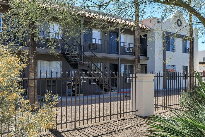 Charming apartment complex with stylish exterior, lush greenery, and secure gated entrance.