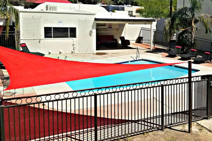 Inviting outdoor pool area featuring stylish sun loungers, a vibrant red shade sail, and lush green landscaping for a perfect retreat.