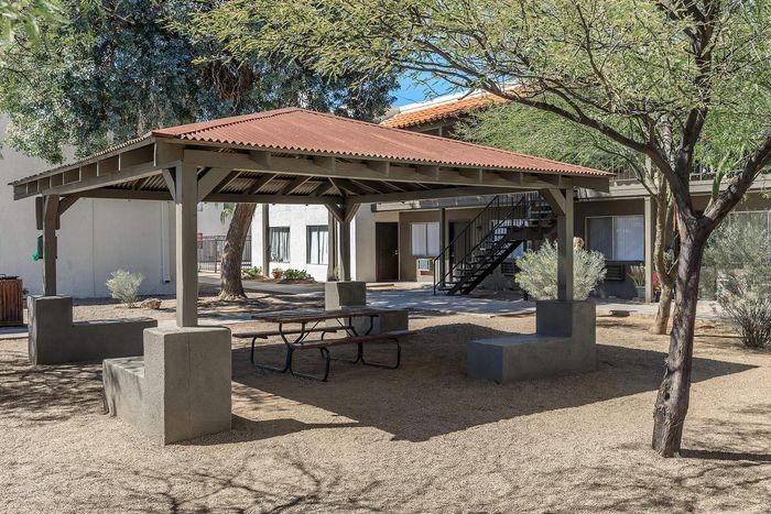 Charming apartment courtyard featuring a shaded gazebo, bench seating, and lush trees creating a tranquil outdoor retreat.