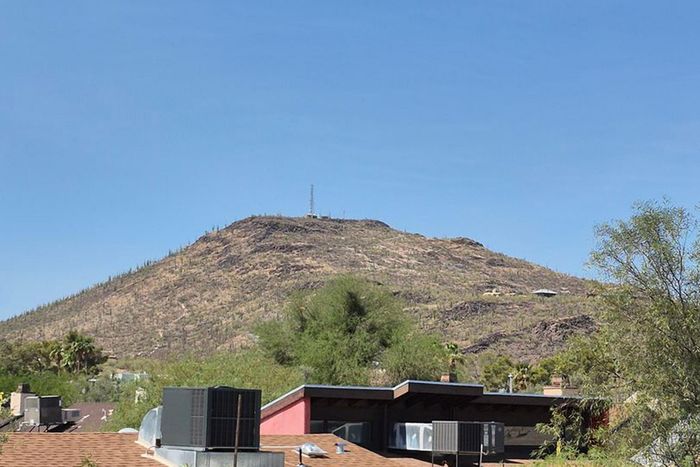 Stunning mountain view with clear blue skies, showcasing a modern home nestled in lush greenery.