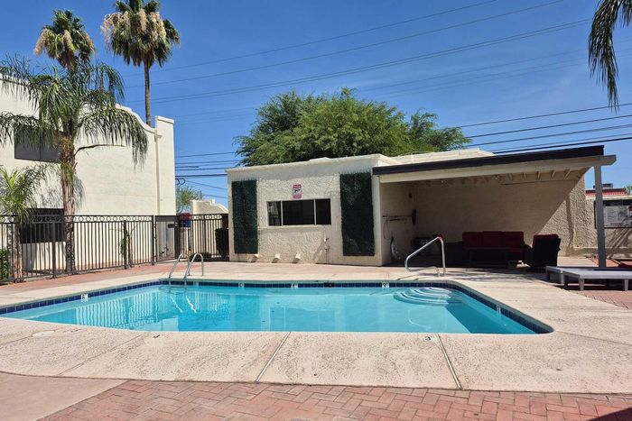 Inviting outdoor swimming pool area with modern seating under a shaded patio, surrounded by lush greenery and palm trees.
