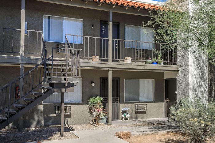 Charming two-story apartment exterior with a private upstairs balcony, surrounded by lush greenery.