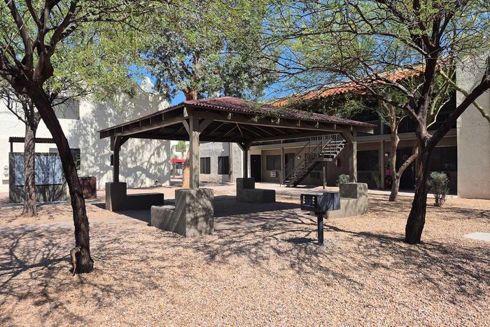 Charming apartment courtyard with shaded seating area, surrounded by lush trees and gravel pathways.