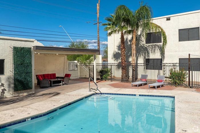 Inviting apartment pool area with lounging chairs, cozy seating, and lush palm trees under a clear blue sky.