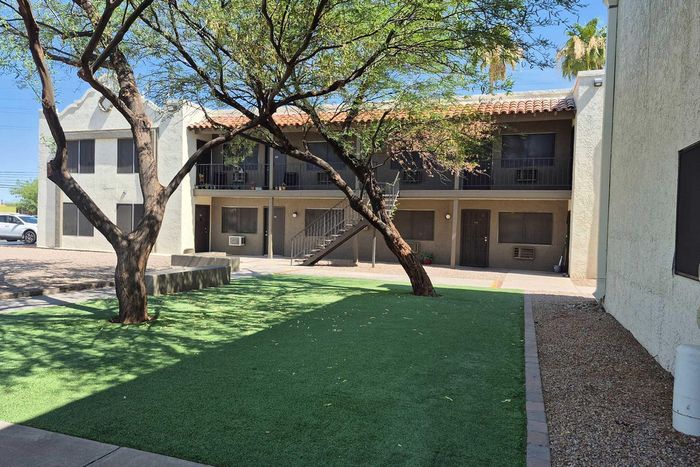 Charming apartment exterior with a lush green courtyard and modern two-story design, perfect for relaxed living.