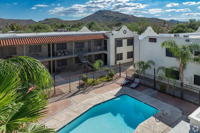 Inviting apartment complex featuring a sparkling outdoor pool with comfortable lounge chairs, set against a backdrop of serene hills and lush greenery.