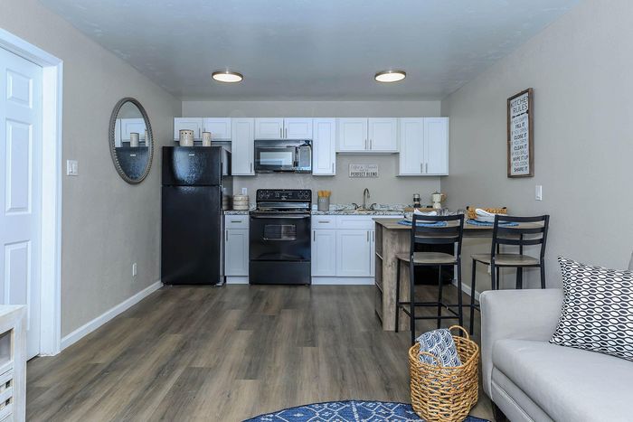 Modern kitchen with sleek white cabinets and black appliances, featuring stylish bar seating and cozy living area accents.