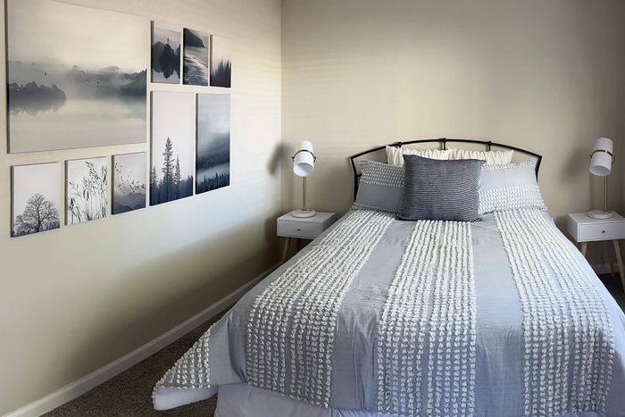 Cozy bedroom featuring a stylishly dressed bed with soft gray and white linens, complemented by modern bedside lamps and artistic wall decor.