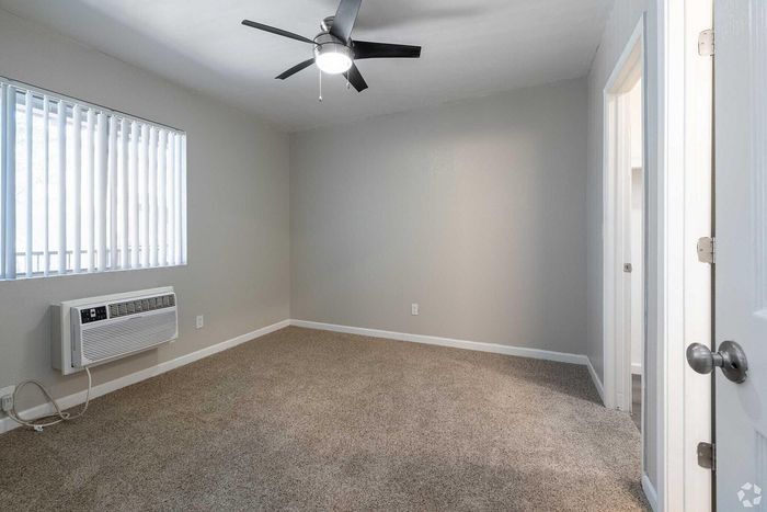 Bright and inviting room with plush carpet, modern ceiling fan, and ample natural light through large window blinds, perfect for a cozy retreat.