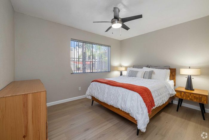 Inviting bedroom with modern ceiling fan, cozy bed, stylish wooden furniture, and ample natural light from the window.