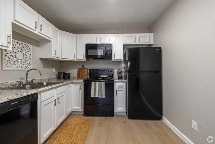 Charming modern kitchen with sleek black appliances, white cabinetry, granite countertops, and elegant wood flooring.
