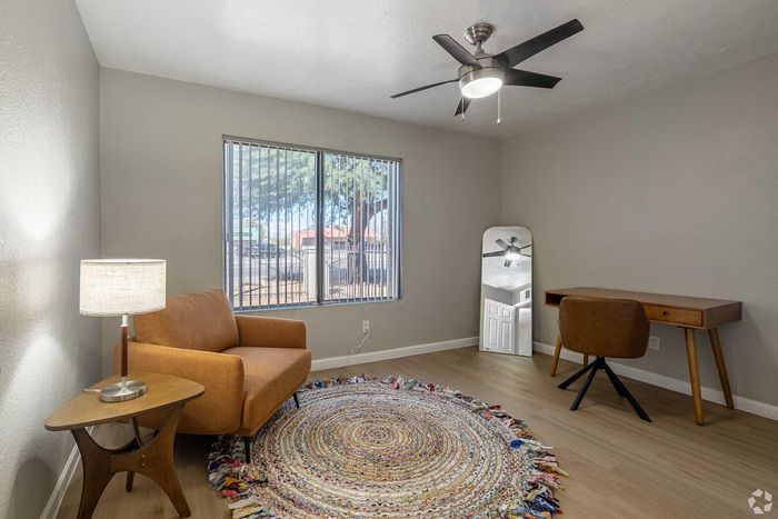 Cozy room with a stylish brown sofa, bright floor-to-ceiling window, chic round rug, and a sleek desk with a modern chair.