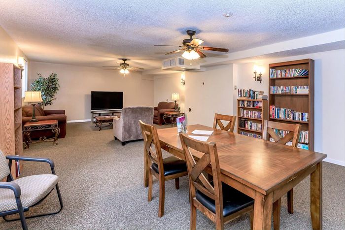 Inviting living area featuring cozy couches, elegant wooden dining set, ceiling fans, and a well-stocked bookcase for a perfect blend of comfort and style.